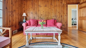 Una habitación acogedora con paredes de madera, un sofá rosa, una mesa blanca y una lámpara azul.