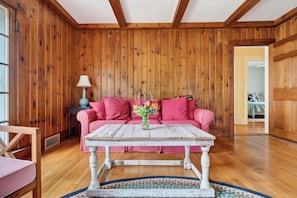 A cozy room with wooden walls, a pink sofa, a white table, and a blue lamp.
