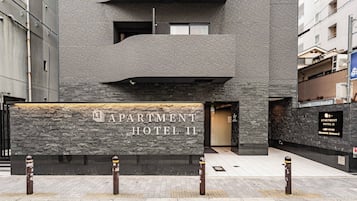 Fachada moderna de edificio con pared de textura de piedra y un letrero que dice 'APARTMENT HOTEL II'.
