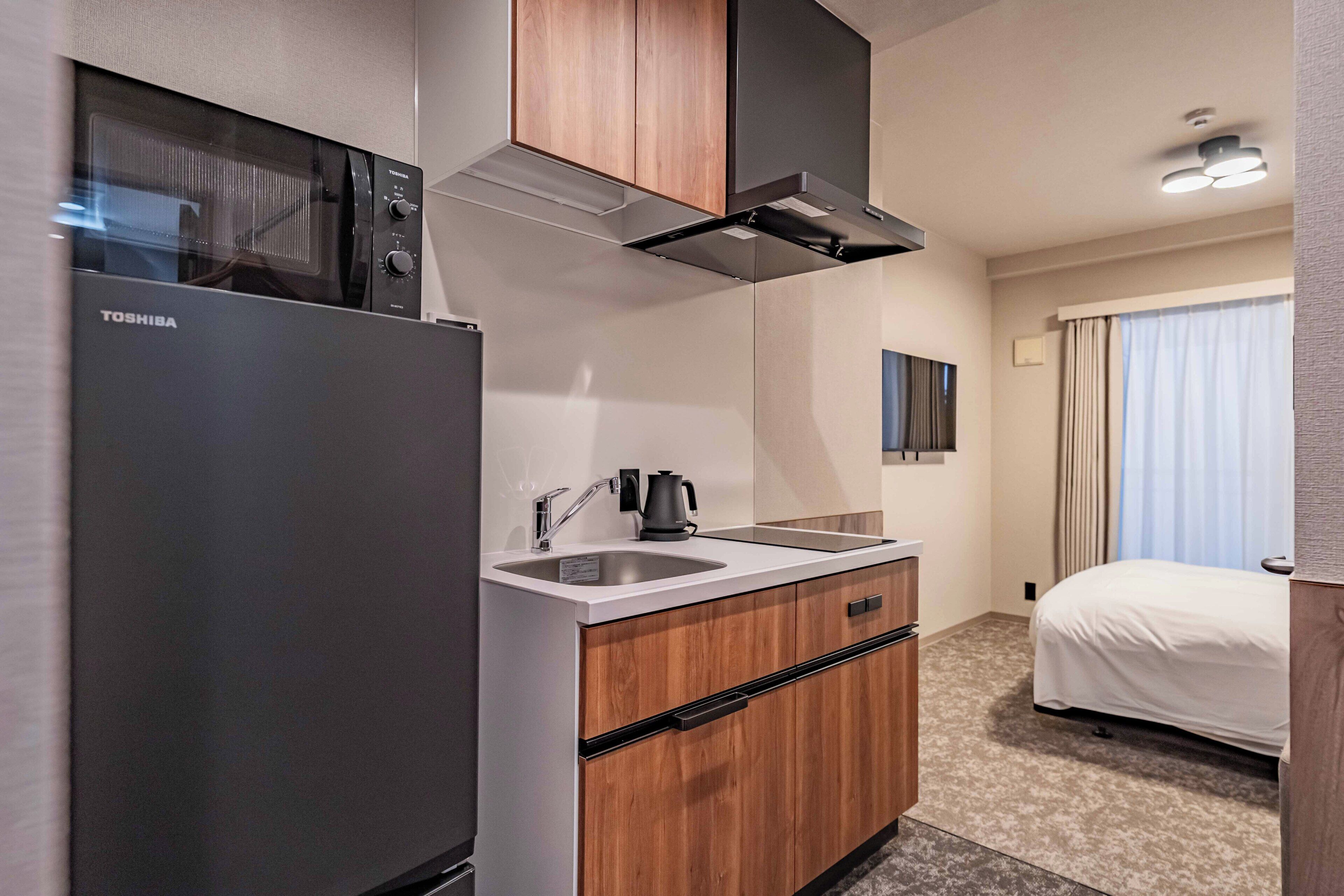 Une chambre d’hôtel moderne dotée d’une kitchenette, comprenant un réfrigérateur, une cuisinière et un évier.