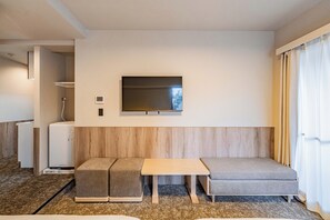 Ein Hotelzimmer mit einer Couch, einem kleinen Tisch, einem an der Wand befestigten Fernseher und einer Minikühlschrank.