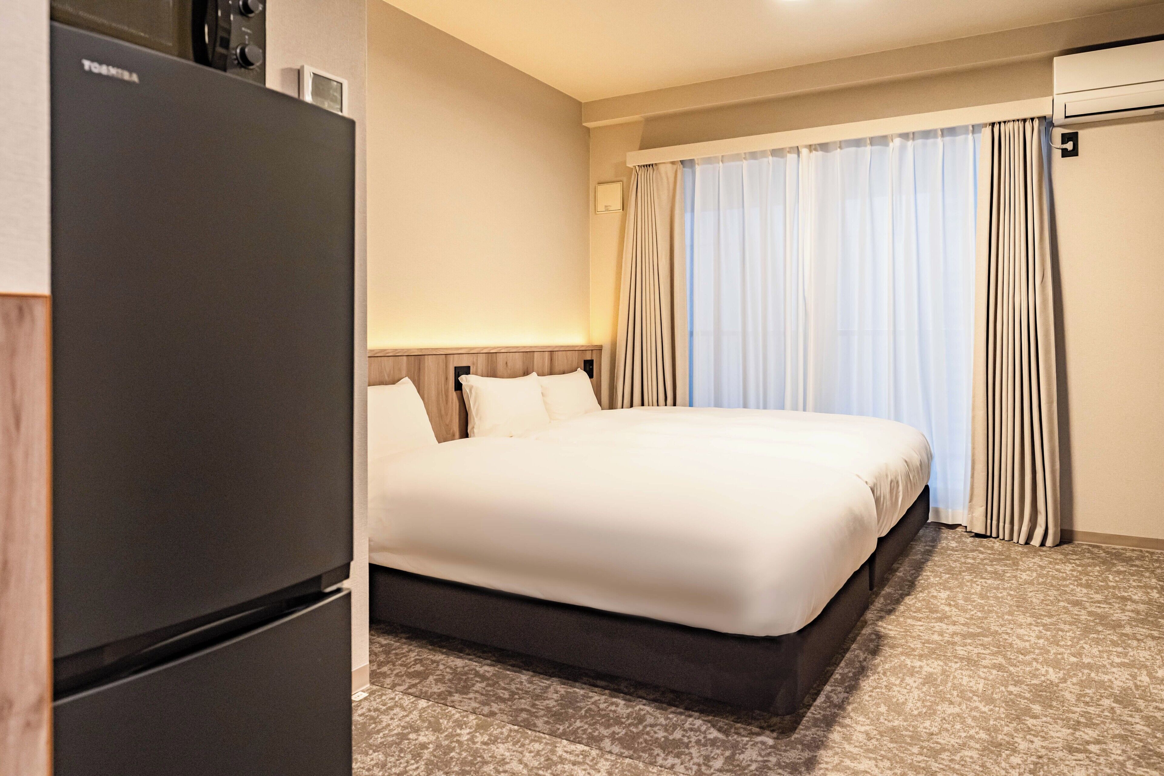 Une chambre d’hôtel avec un lit, un réfrigérateur et une fenêtre avec des rideaux.