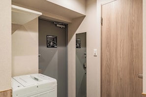 Un couloir étroit avec une porte grise, un appareil blanc et une porte en bois.