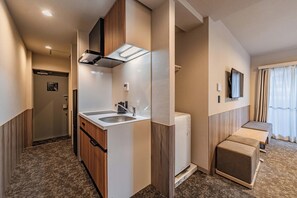 Ein Hotelzimmer mit Küchenzeile, einer integrierten Waschmaschine, einem an der Wand befestigten Fernseher und einer Sitzecke mit einer Bank.