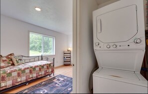 A bedroom with a bed, a window, a laundry machine, and a shelf with items. - Pleasant 2-bedroom with an upstairs loft cabin in cozy Soldotna for your getaway (Kasilof)