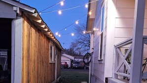 A narrow driveway leading to a garage with a wooden exterior and a white building with a lattice fence. - Bluish Cabin (Bucoda)