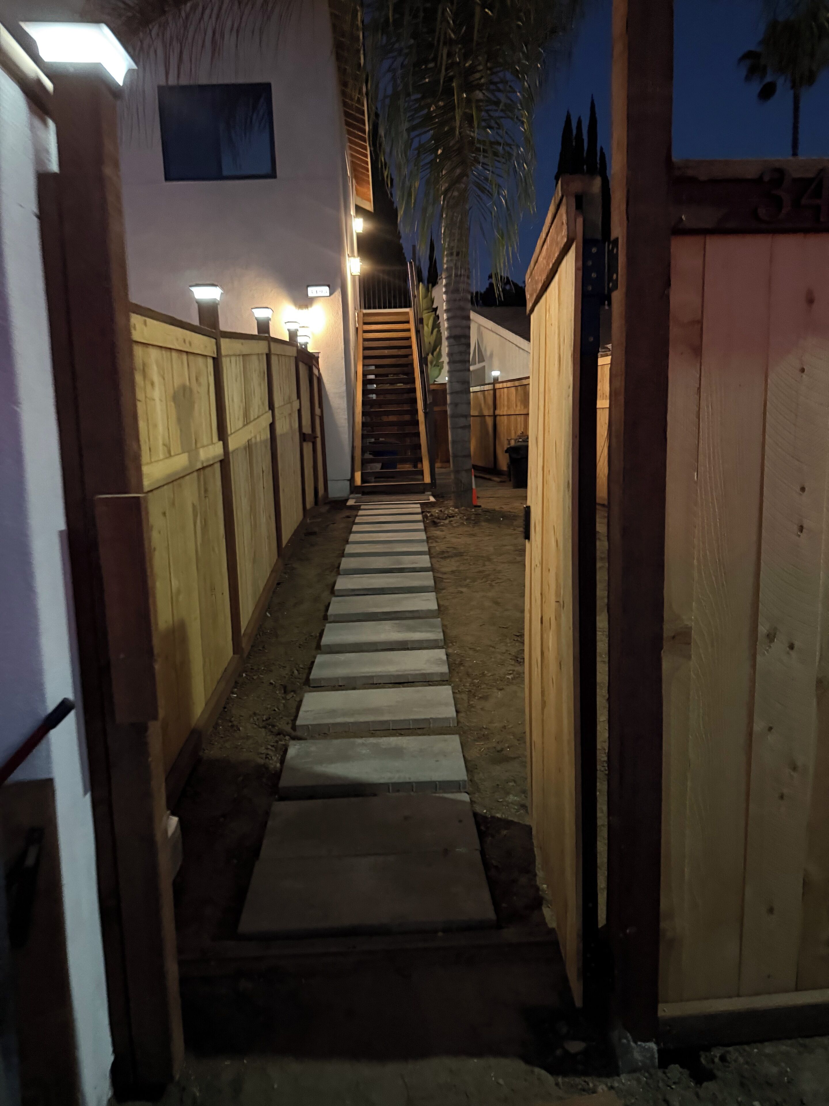 Un chemin menant à une porte en bois, bordé de murs et d’un escalier.