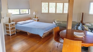 Une pièce avec un lit, une table et une chaise. Il y a des fenêtres et une porte.