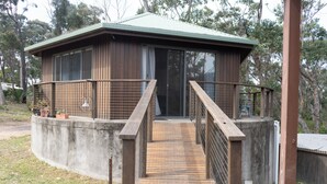 Une cabane en bois dotée d’un balcon, d’un mur de soutènement en béton et d’une terrasse en bois menant à l’entrée.