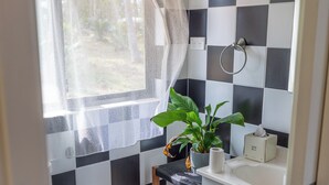 Une petite salle de bain avec un carrelage à motifs, des toilettes, un lavabo avec un distributeur de serviettes et une plante en pot.