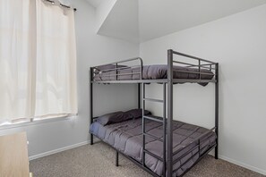 A bunk bed with a metal frame, grey bedding, and a window with white curtains.