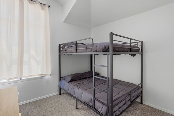 A bunk bed with a metal frame, grey bedding, and a window with white curtains.