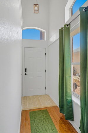 A hallway with a white door, a green rug, and a window with green curtains.