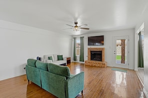 A living room with a green sofa, a fireplace, and a ceiling fan.