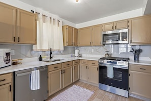 A kitchen with wooden cabinets, a stainless steel dishwasher, a stove, and a microwave.