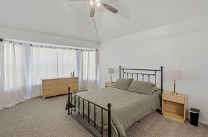 Ein Schlafzimmer mit einem Bett, Nachttischen, einem Schminktisch, einem Deckenventilator und einem Fenster mit Vorhängen.