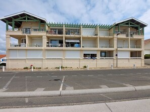 A multi-story building with balconies, a covered walkway, and a parking lot in front. - les Goelands by Interhome (Mimizan)