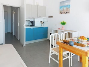Ett modernt kök med blå skåp, ett matbord med stolar och en tavla som föreställer en strandscen.