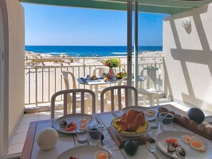 A dining table with plates of food, a glass of water, and a view of the beach and ocean. - les Goelands by Interhome (Mimizan)
