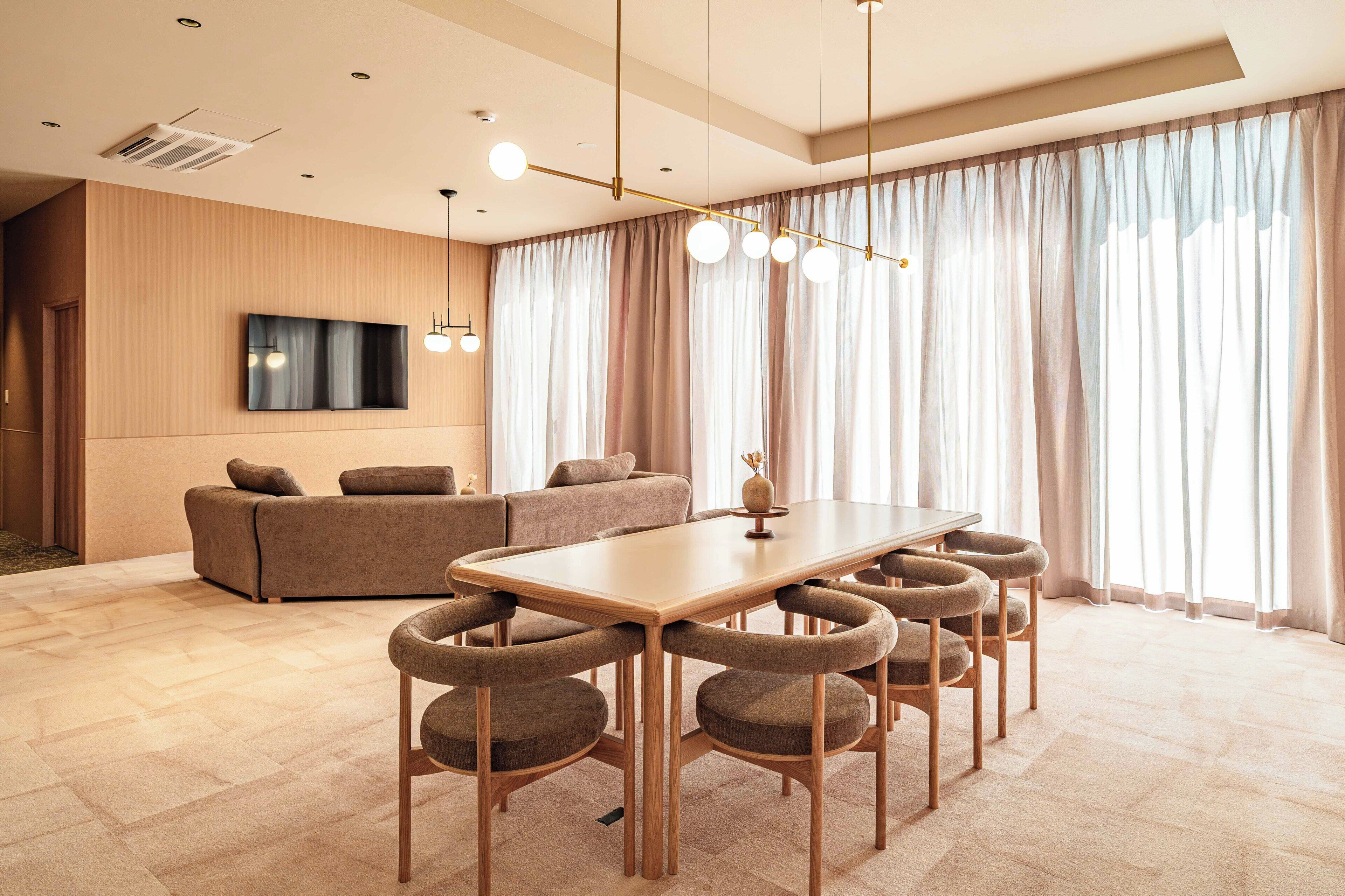 A modern living room with a sofa, a TV mounted on the wall, and a dining area with a table and chairs.
