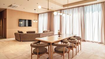 A modern living room with a sofa, a TV mounted on the wall, and a dining area with a table and chairs.