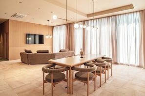A modern living room with a sofa, a TV mounted on the wall, and a dining area with a table and chairs.