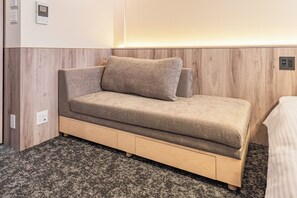 A modern, compact sofa with storage drawers against a wooden wall, a power outlet, and a carpeted floor. - Apartment Hotel 11 Shinsaibashi 9 (Osaka-shi)