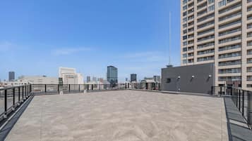 A rooftop terrace with a view of a city skyline, featuring modern buildings and a clear sky.