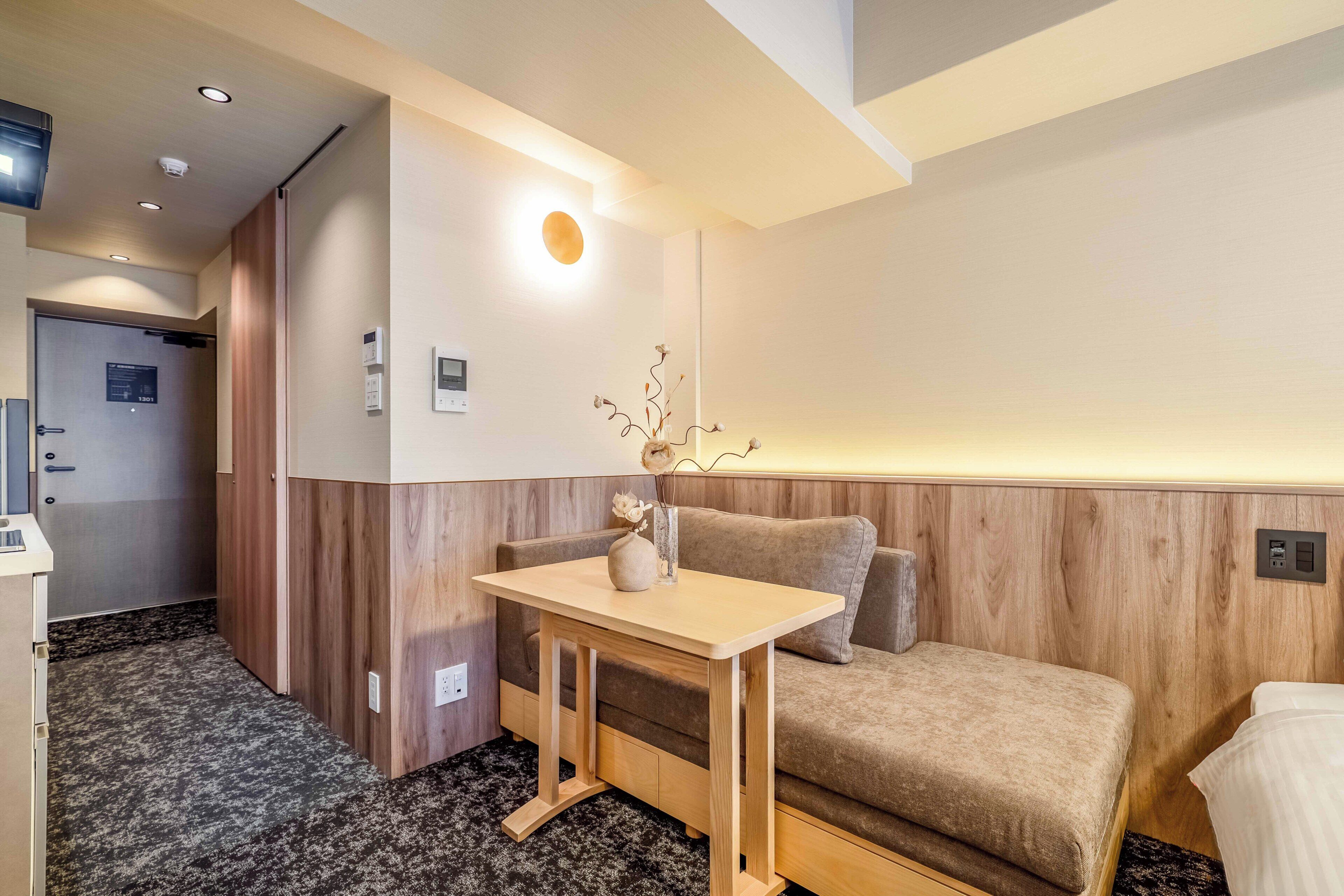 A hotel room with a wooden accent wall, a small table with a vase, a sofa, and a bed.