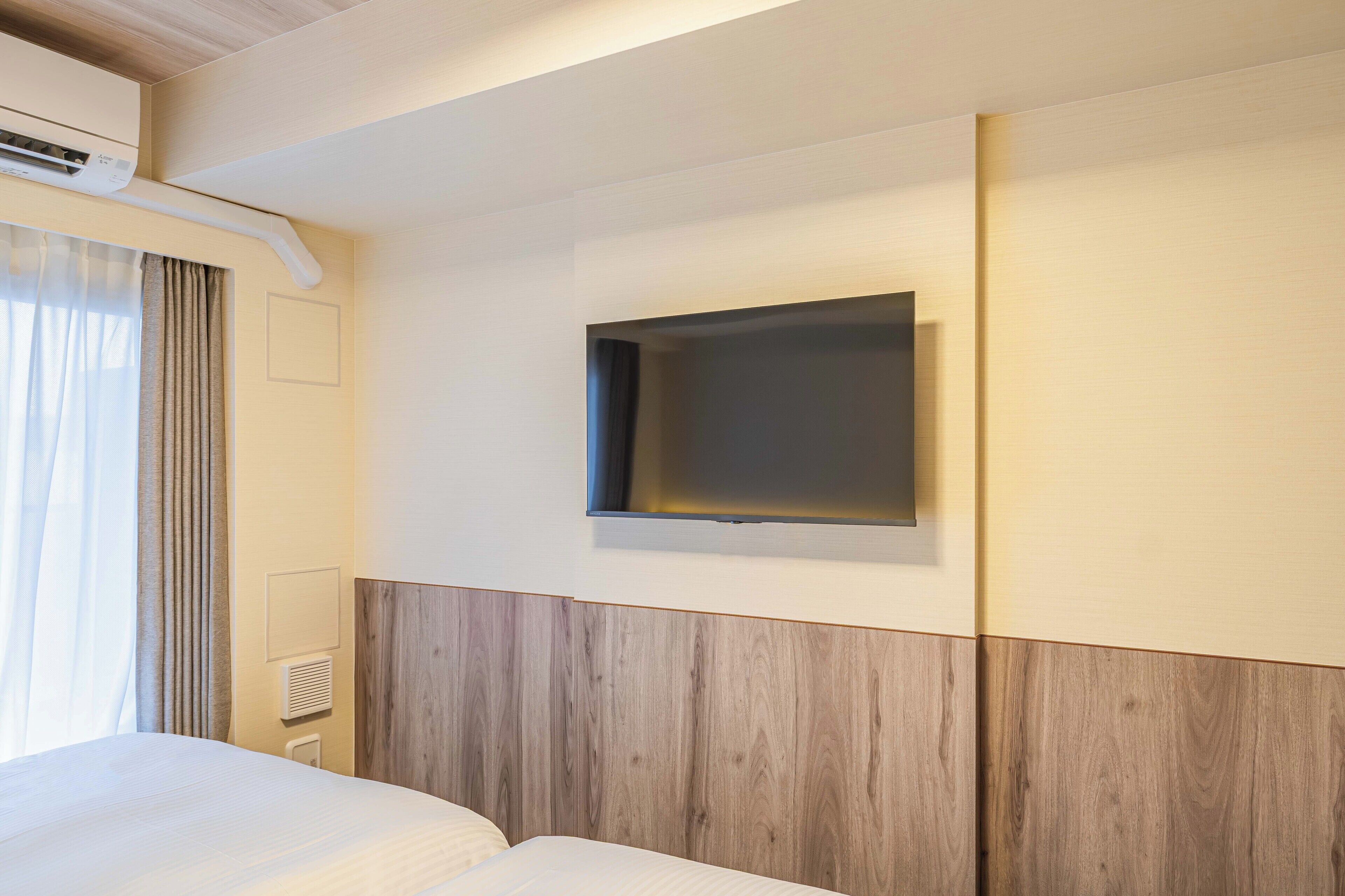 A hotel room with a bed, a wall-mounted TV, and a window with curtains.
