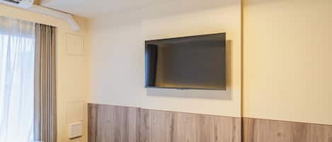 A hotel room with a bed, a wall-mounted TV, and a window with curtains.