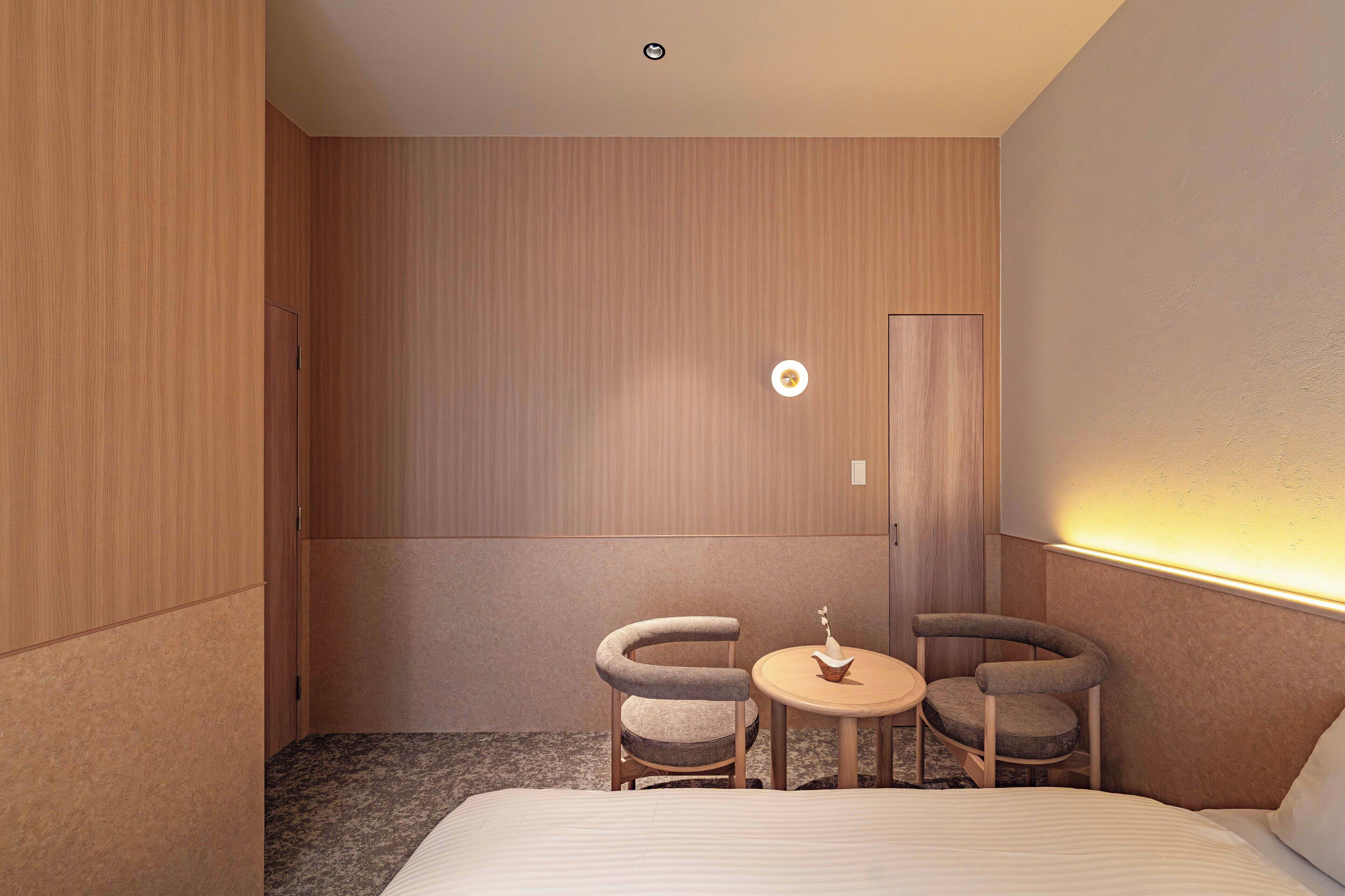 A hotel room with a bed, two chairs, a small table, and a door.