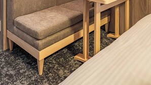 Um quarto pequeno e acolhedor com um sofá, uma mesa de madeira e um candeeiro fixado na parede.