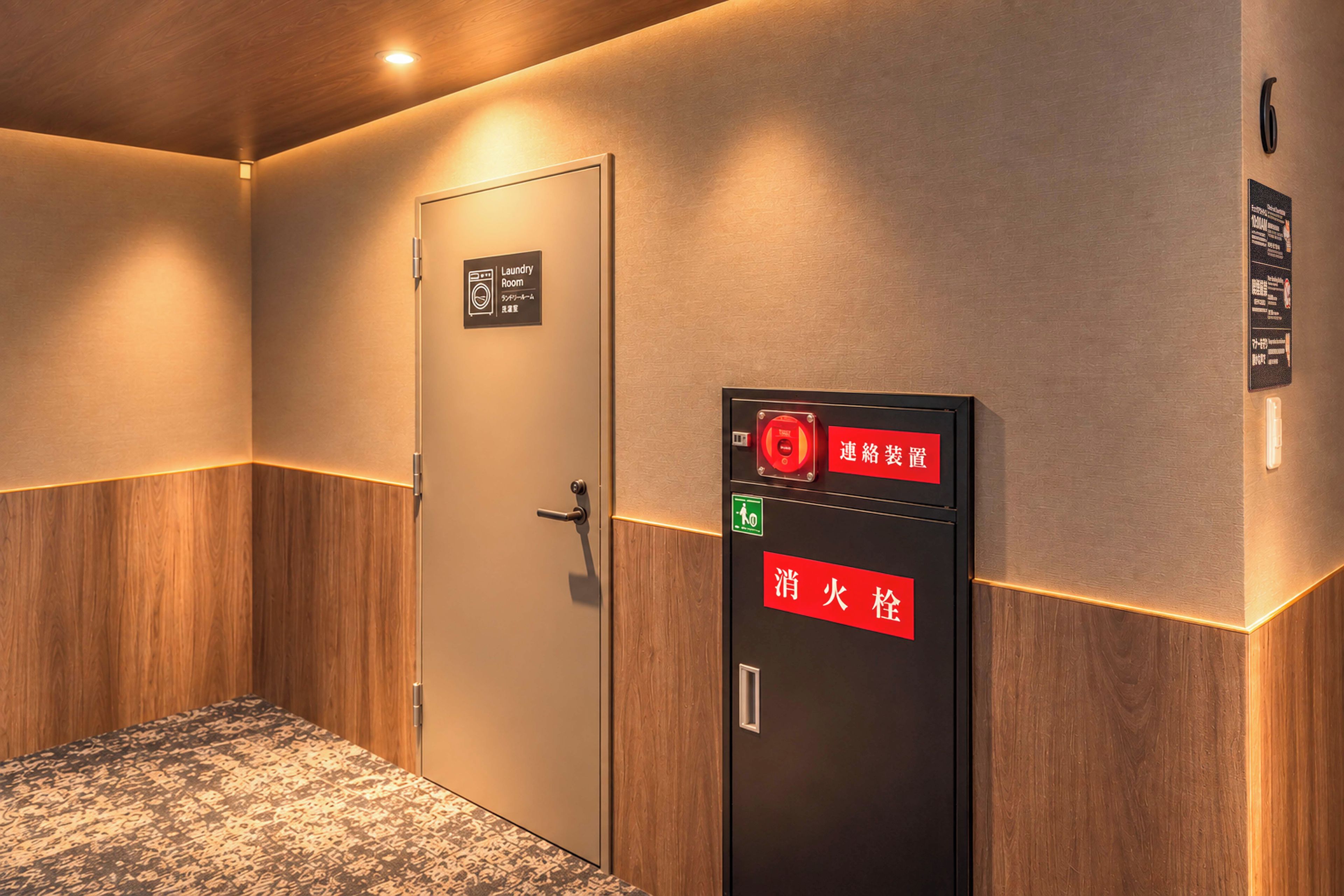 Une chambre d’hôtel avec une porte en bois, un détecteur d’incendie fixé au mur et un panneau indiquant l’emplacement de la buanderie.