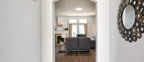 Ein Flur, der in ein Wohnzimmer mit Kamin, einer Couch und einem Ziertepiegel führt.