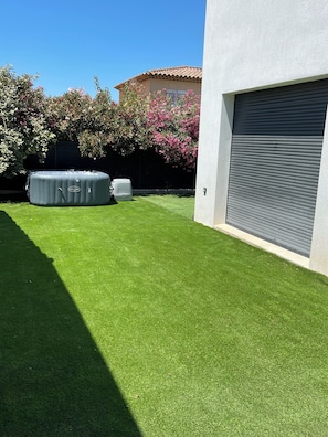 Um quintal com grama sintética, uma banheira de hidromassagem e uma porta de garagem.