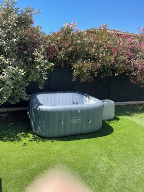 A gray inflatable hot tub with a control panel, situated on artificial grass in a backyard with a dark fence and flowering plants. - Maison spacieuse 4 chambres climatisées proche aéroport,gare tgv et plages (Les Pennes-Mirabeau)