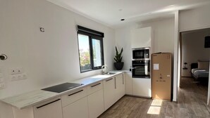 Una cocina moderna con armarios blancos, horno empotrado y un amplio ventanal.