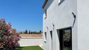 Un edificio moderno con fachada blanca y techo de tejas, un patio cubierto de césped y un cielo azul despejado.