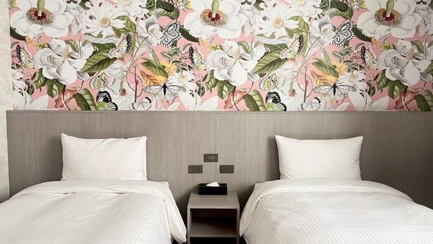 A hotel room with two beds, a nightstand, and a floral wallpaper. - starshotel (Taichung)