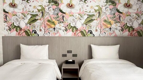 A hotel room with two beds, a nightstand, and a floral wallpaper.