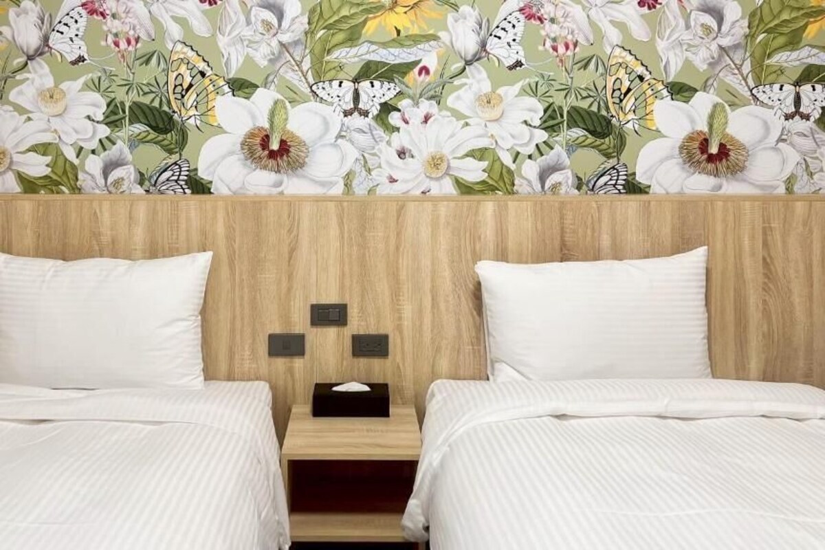 A hotel room with two beds, a wooden headboard, and a floral wallpaper.