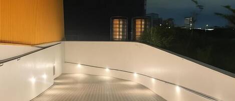 Un balcón con suelo de baldosas y barandilla, con vistas a un paisaje urbano nocturno.