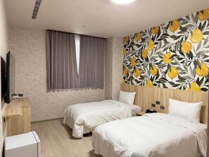 A hotel room with two beds, a flat-screen TV, a small desk, and a wall with a fruit pattern.
