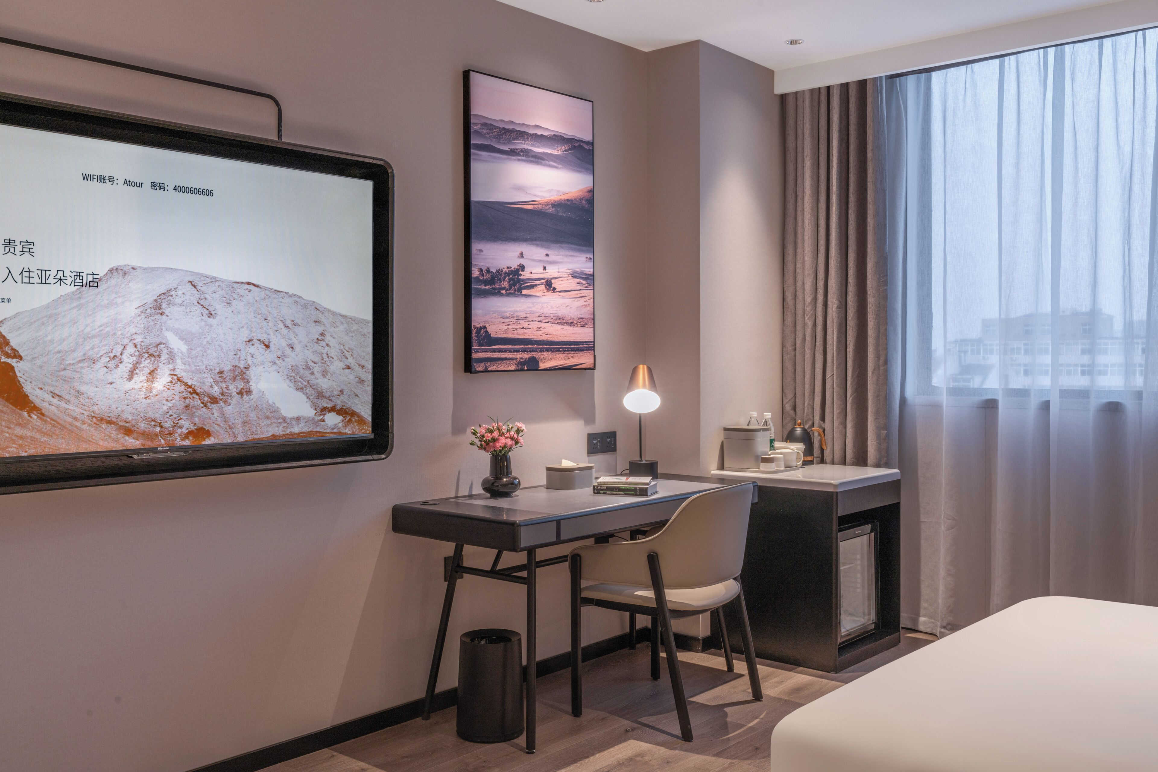 Habitación de hotel con una cama, un escritorio con silla, televisor, un cuadro enmarco, lámpara y ventana con cortinas.