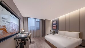 Habitación de hotel moderna con una cama grande, un escritorio, una silla, una pantalla de televisión y una ventana con cortinas.