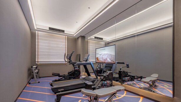Un gimnasio con equipo de ejercicio, un espejo grande y una pantalla que muestra una imagen de una montaña.