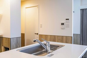 Eine moderne Küche mit Spüle aus Edelstahl, einer Tür im Hintergrund und einem an der Wand befestigten Thermostat.
