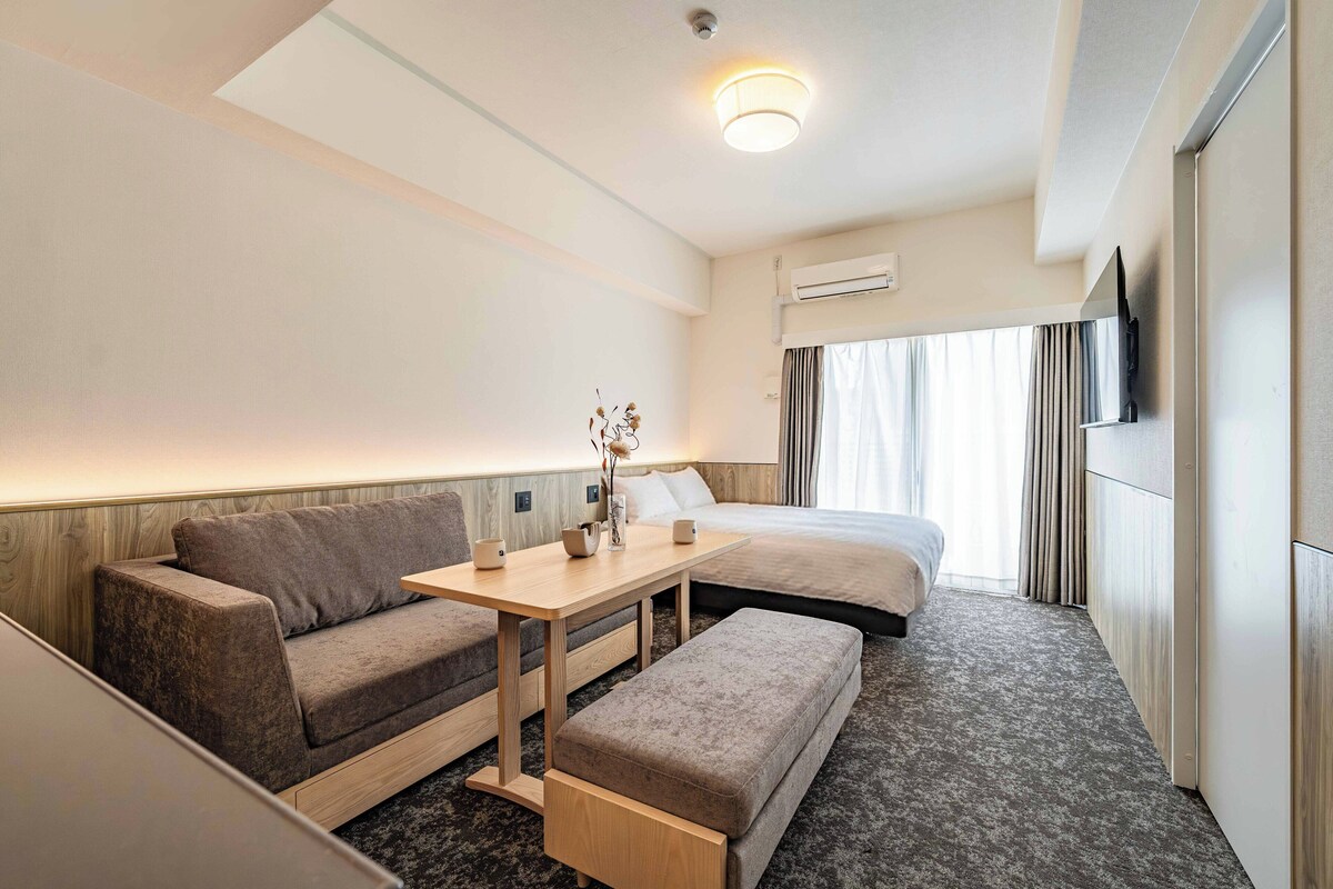 Ein Hotelzimmer mit Sofa, einem kleinen Tisch, einer Bank, einem Bett, einer Klimaanlage und einem Fenster mit Vorhängen.