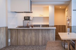Una cocina moderna con microondas integrado, estufa a gas y refrigerador pequeño. Hay una encimera de madera y un lavamanos blanco.